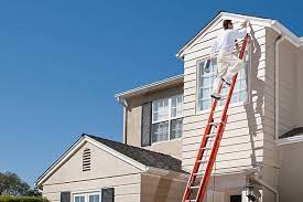 man painting siding on exterior of home